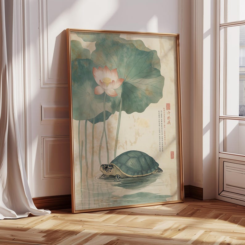 May include: A framed art print featuring a turtle in water beneath a lotus flower and large leaves. The artwork has a vintage aesthetic with soft colors and Japanese text. The frame is gold-toned, and the print is leaning against a wall.