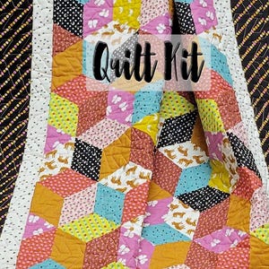 May include: A colourful quilt kit with a geometric design. The quilt features a variety of patterns, including polka dots, butterflies, and tiger prints, in shades of pink, yellow, blue, and orange. The words "Quilt Kit" are displayed on the quilt.