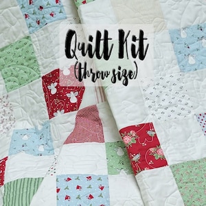 May include: A quilt kit in a throw size with a white background and squares of red, green, blue, and white patterned fabric. The text "Quilt Kit (throw size)" is printed on the quilt.
