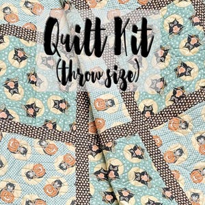 May include: A quilt kit featuring a black cat and pumpkin design on a blue and brown background. The kit is throw size and includes the text "Quilt Kit (throw size)".
