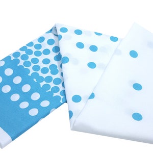 May include: A folded piece of blue and white fabric with a polka dot pattern. The fabric has a gradient of blue polka dots on one side and a scattered pattern of blue polka dots on the other side.