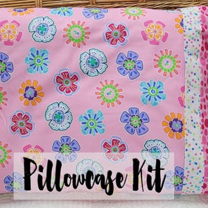 May include: A pink pillowcase kit with a floral print and a pink, white, and polka dot trim. The pillowcase kit is labeled "Pillowcase Kit".