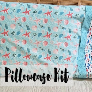 May include: A pillowcase kit with a light blue fabric patterned with red starfish, seashells, and teal details. The kit includes a second fabric with a pattern of small fish in blue, red, and white. The words "Pillowcase Kit" are printed on the front.
