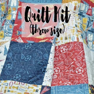 May include: A quilt kit featuring a sports theme with a blue, red and white colour scheme. The kit includes fabric squares with various sports-related patterns, including basketballs, baseballs, footballs and other sports equipment. The text "Quilt Kit (throw size)" is displayed on the image.