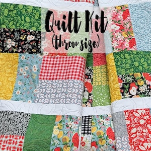 May include: A quilt kit in a throw size, featuring a patchwork design with various colorful fabrics. The fabrics include red and white gingham, floral patterns, and green and black patterns. The quilt kit is labeled "Quilt Kit (throw size)".