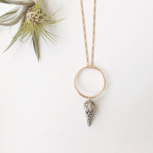 Puede incluir: Un collar de cadena dorada con un colgante circular y una piedra de jaspe dálmata colgando de la parte inferior.