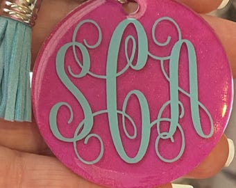 May include: Pink glitter keychain with a blue monogram of the letters "SGA". The keychain has a blue tassel.