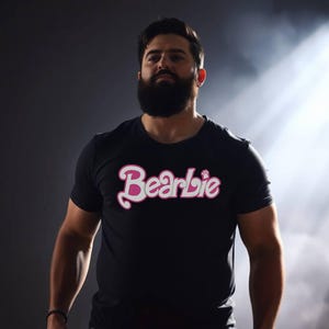 Könnte beinhalten: Ein Mann mit Bart trägt ein schwarzes T-Shirt mit dem Wort "Bearbie" in rosa und weißen Buchstaben.