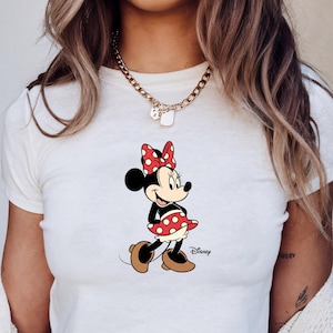 May include: White crop top with a Minnie Mouse graphic. The cartoon character is wearing a red and white polka dot dress and bow. The Disney logo is printed on the shirt.