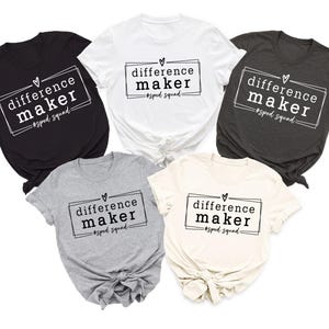 May include: Five short-sleeved t-shirts in black, white, charcoal, grey, and cream. Each shirt displays the text "difference maker" within a rectangular frame, with a heart above and "#sped squad" below.
