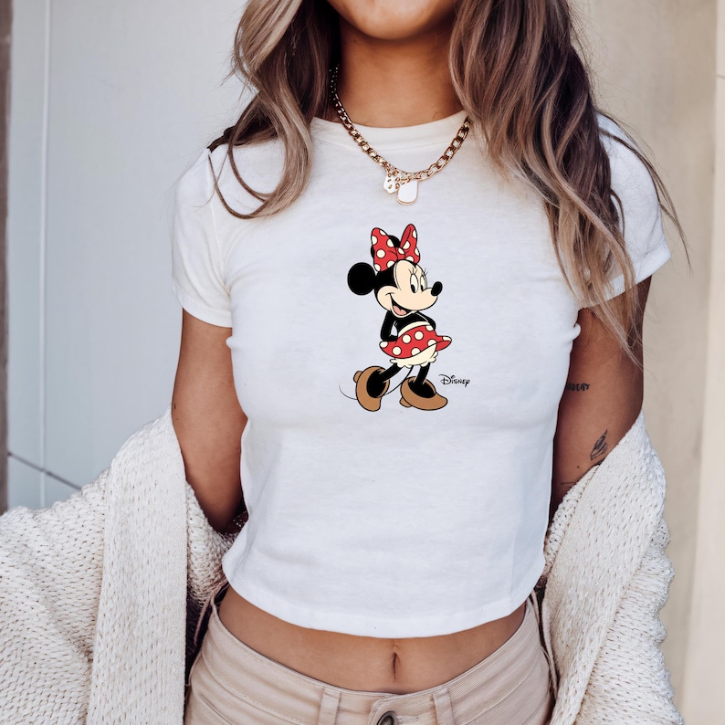 May include: White crop top with a Minnie Mouse graphic. The cartoon character is wearing a red and white polka dot dress and bow. The Disney logo is printed on the shirt.