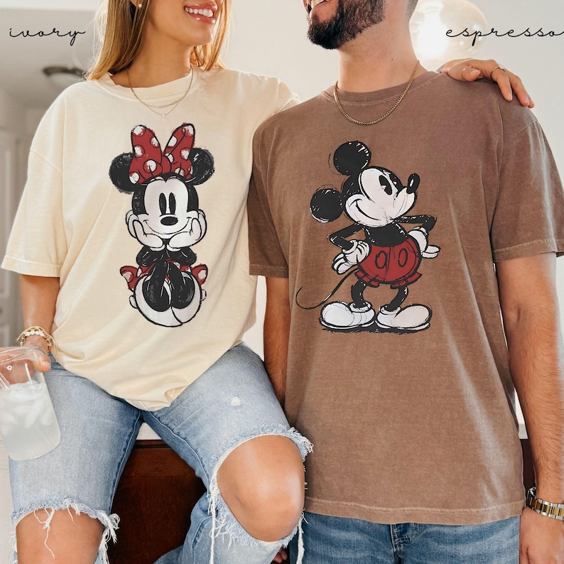Puede incluir: Dos camisetas de manga corta, una marfil y otra espresso, con gr&aacute;ficos de Mickey y Minnie Mouse. La camiseta de Minnie Mouse es marfil, y la camiseta de Mickey Mouse es espresso. Ambas camisetas tienen un aspecto vintage y desgastado, con los personajes en blanco y negro.