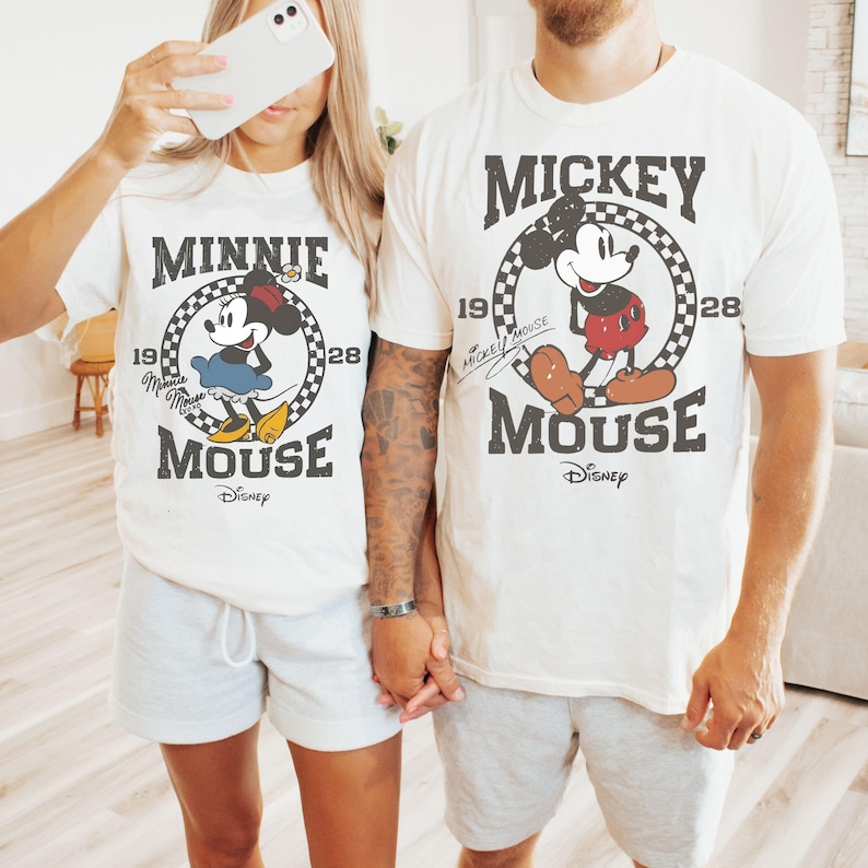 Puede incluir: Camisetas blanquecinas con Mickey y Minnie Mouse. Cada camiseta tiene un gr&aacute;fico circular con la imagen del personaje, el texto "MICKEY MOUSE" o "MINNIE MOUSE" y el logotipo de Disney. Las camisetas se combinan con pantalones cortos grises.
