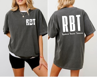 May include: Charcoal gray t-shirt with white text. The front of the shirt displays "RBT" with the name "Kate" below it. The back of the shirt has the letters "RBT" and the words "Registered Behavior Technician".