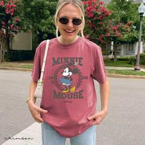 Puede incluir: Una camiseta de color carmes&iacute; con un dise&ntilde;o de Minnie Mouse. El dise&ntilde;o incluye el texto "MINNIE MOUSE" en un estilo vintage, con el a&ntilde;o "1928" y el logotipo de Disney. La camiseta es de manga corta y de corte holgado.