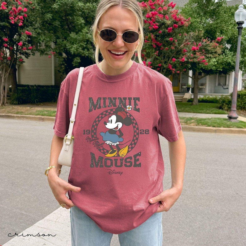 Puede incluir: Una camiseta de color carmes&iacute; con un dise&ntilde;o de Minnie Mouse. El dise&ntilde;o incluye el texto "MINNIE MOUSE" en un estilo vintage, con el a&ntilde;o "1928" y el logotipo de Disney. La camiseta es de manga corta y de corte holgado.
