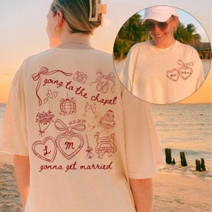 May include: A cream-coloured t-shirt featuring a red graphic design. The design includes the text "going to the chapel gonna get married" and wedding-themed illustrations. A smaller image shows a person wearing the shirt.