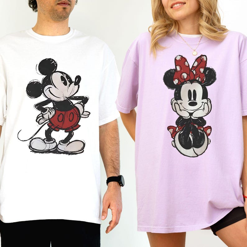 Puede incluir: Dos camisetas con personajes de Disney. Una es blanca con un boceto de Mickey Mouse con pantalones cortos rojos. La otra es de color lila claro con un boceto de Minnie Mouse con un lazo rojo de lunares. Ambas camisetas son de manga corta.