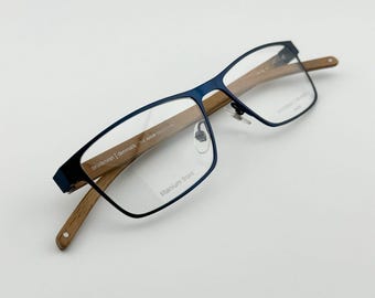 May include: Blue titanium frame eyeglasses with a wooden temple arm. The frame has the text "prodesign denmark" and "titanium front" printed on it.