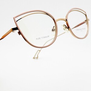 Puede incluir: Gafas de color oro rosa con un diseño de montura angular único. Las gafas presentan una estructura de doble montura con el texto "PURE TITANIUM" y "FACE A FACE PARIS" visibles en las lentes. Las monturas tienen una estética moderna y elegante.