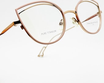 May include: Rose gold-colored eyeglasses with a unique, angular frame design. The glasses feature a double-rimmed structure with the text "PURE TITANIUM" and "FACE A FACE PARIS" visible on the lenses. The frames have a modern, stylish aesthetic.