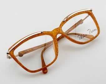 May include: Vintage Paloma Picasso eyeglasses with a unique giraffe-like pattern in shades of brown and gold. The frames have a rectangular shape with a gold trim and clear lenses. The brand name is visible on the lens.