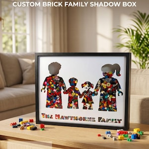 May include: A black rectangular shadow box frame containing a white insert with four cutout silhouettes of toy figures filled with colorful plastic building bricks. The text THE HAWTHORNE FAMILY is printed in a brick-patterned font at the bottom.