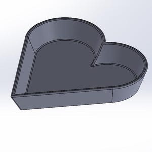 May include: A gray heart-shaped mold for baking or crafting. The mold is made of a smooth, hard material and has a slightly rounded bottom.