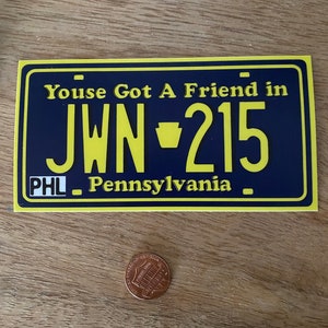May include: A yellow and blue Pennsylvania license plate sticker with the text "Youse Got A Friend in JWN-215" and "PHL Pennsylvania".