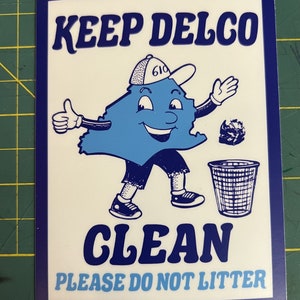 May include: A blue and white sticker with the text "Keep Delco Clean" and a cartoon character of a blue state with a white hat and a trash can. The text "Please do not litter" and "@primitiveshirts" are also on the sticker.