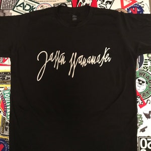 May include: A black t-shirt with a white signature that reads "Jaffa Wannamaker" printed on the front.
