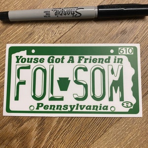 May include: Green and white novelty license plate with the text "Youse Got A Friend in FOL-SOM Pennsylvania" and the number "610".