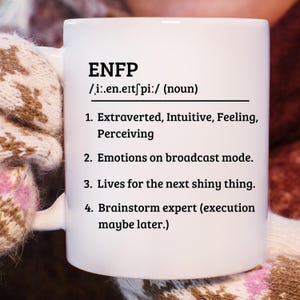 May include: White ceramic mug with the text "ENFP" in bold black letters, followed by a phonetic pronunciation and a definition. The mug also lists four characteristics of the ENFP personality type.