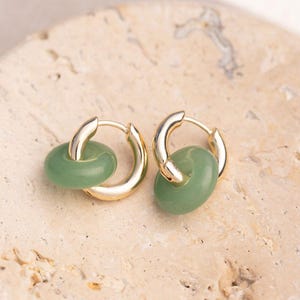 May include: A pair of gold hoop earrings with a green stone accent. The earrings are simple and elegant, and would make a great gift for any occasion.