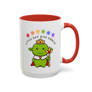 May include: White ceramic mug with a red rim and handle. The mug features a cartoon illustration of a green goblin king with a crown, holding a golden staff. The text "Little Gay Dice Goblin" is printed in black around the goblin, with rainbow dice above the text.