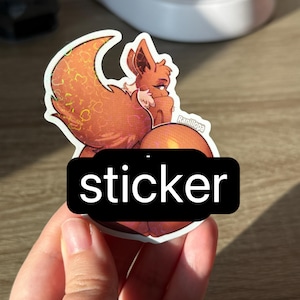 May include: A die-cut sticker featuring a brown, fox-like creature with large ears and a fluffy tail, rendered in a stylised illustration with a holographic heart pattern overlay. The sticker includes the text Ranillopa printed in white.