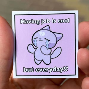 Könnte beinhalten: Ein Aufkleber mit einer lila Katze mit einem gebrochenen Herzen auf der Stirn, die weint. Der Text auf dem Aufkleber lautet "Einen Job zu haben ist cool, aber jeden Tag??"