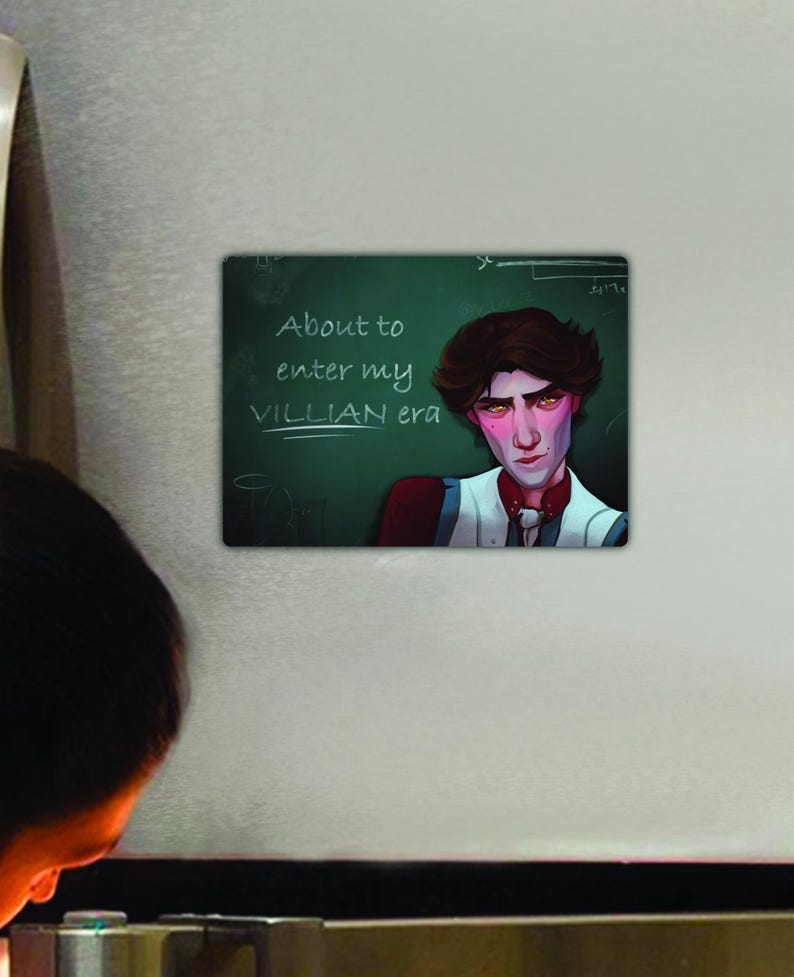 May include: A green chalkboard with white writing that says "About to enter my VILLIAN era". A young man with dark hair and a serious expression is standing in front of the chalkboard. He is wearing a white shirt with a red vest and a black bow tie.
