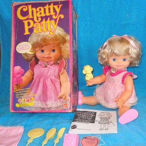 May include: Vintage Chatty Patty doll in a pink dress, with accessories and original box. The box features the doll's image and the text "Chatty Patty". Accessories include a comb, brush, and a small pink block. The doll has blonde hair and blue eyes.