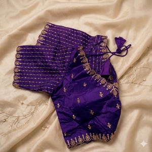 Può includere: Una vivace camicetta viola con ricami dorati intricati lungo lo scollo e le maniche. La camicetta presenta un bordo smerlato e delicate perline, creando un design elegante e dettagliato. Il tessuto ha una lucentezza sottile, che contribuisce al suo aspetto lussuoso.