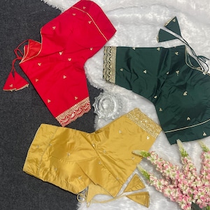 May include: Three short-sleeved blouses in red, dark green, and mustard yellow. Each blouse features scattered small embroidered floral motifs, a scalloped hem with gold metallic thread detailing, and thin tie-up strings with triangular tassels.
