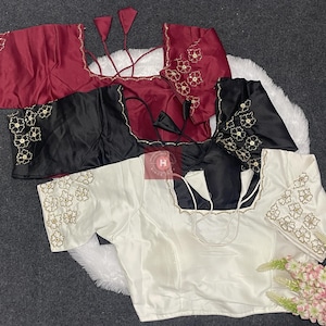 May include: Three short-sleeved blouses in maroon, black, and white, each featuring a square neckline and floral embroidery on the sleeves. The garments include thin tie-up strings at the back and a small red square logo in the center.