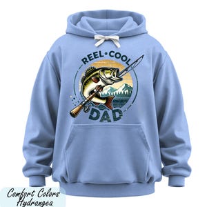 A blue hoodie with a graphic design featuring a fish and the text "REEL. COOL. DAD" printed on it.