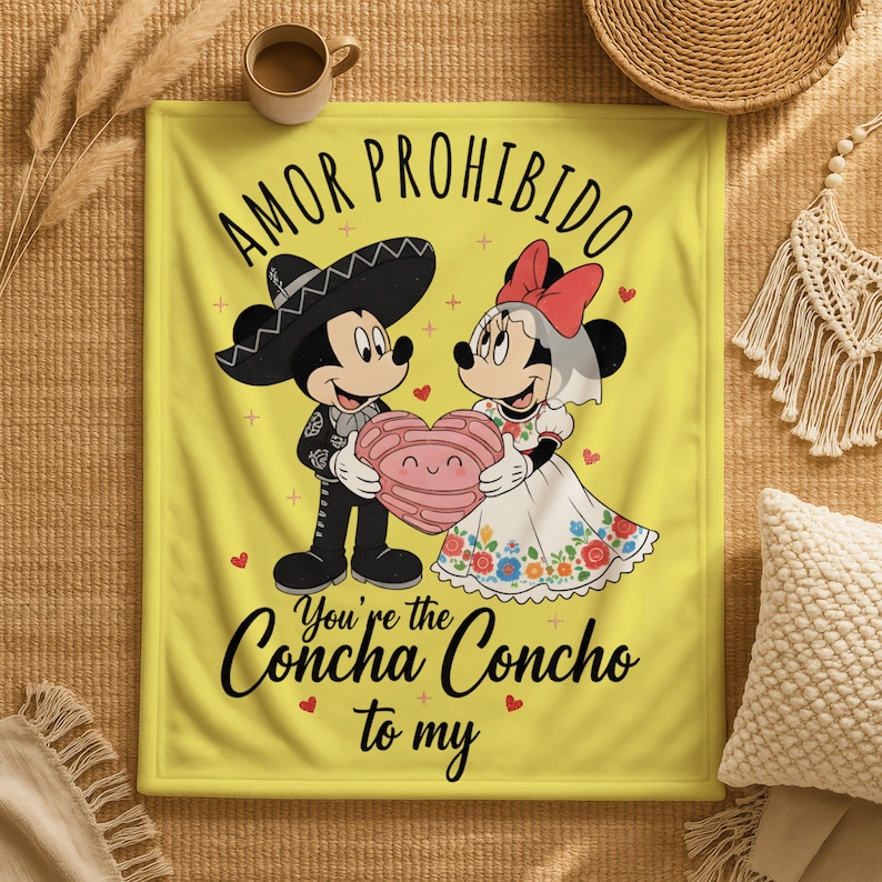 a yellow blanket with a cartoon illustration of Mickey Mouse and Minnie Mouse, along with text that says "Amor Prohibido" and "You're the Concha Concho to my".