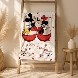 A towel with a cartoon image of Mickey Mouse and Minnie Mouse sharing a kiss, surrounded by hearts, and the text "Love You" on it.