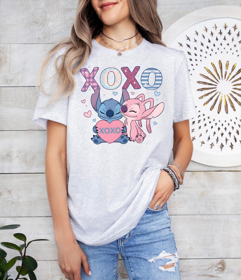 A woman wearing a white t-shirt with a graphic design featuring two cartoon characters, one pink and one blue, along with the text "XOXO" and a heart.