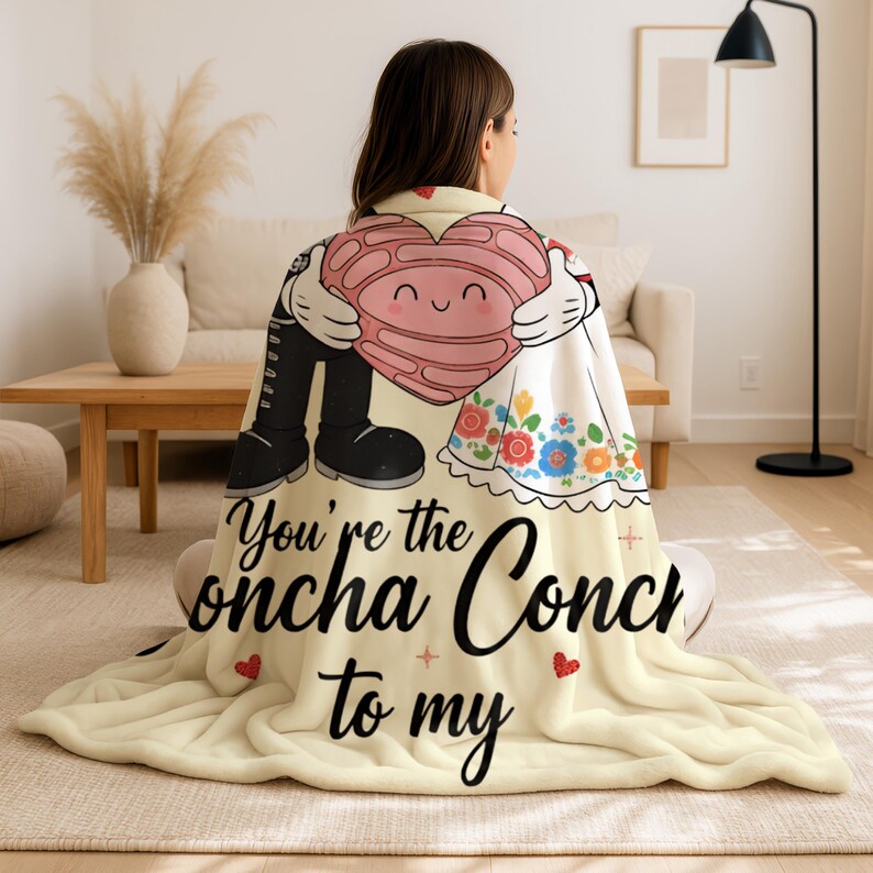 A woman sitting on the floor with a blanket featuring a cartoon character holding a heart and the text "You're the Onchka Conch to my".