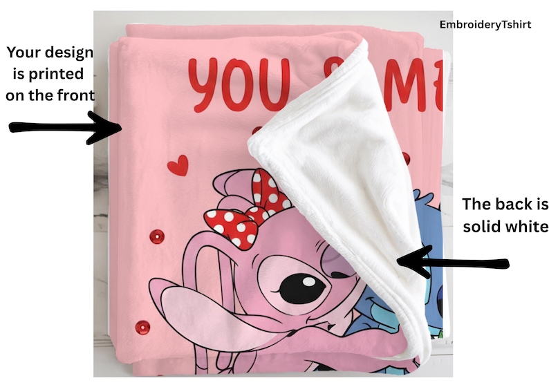 a pink blanket with a cartoon character design, including a bow and hearts. The blanket is folded over itself, revealing the back, which is solid white. The blanket is printed on the front, and the back is solid white.