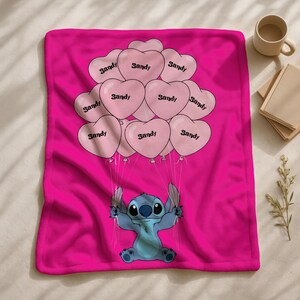 A pink blanket with a cartoon character, likely Stitch, surrounded by heart-shaped balloons labeled with the word "Sandy".