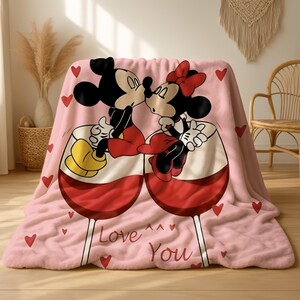 A pink blanket with a cartoon image of Minnie Mouse and Mickey Mouse sitting together and kissing, surrounded by hearts.